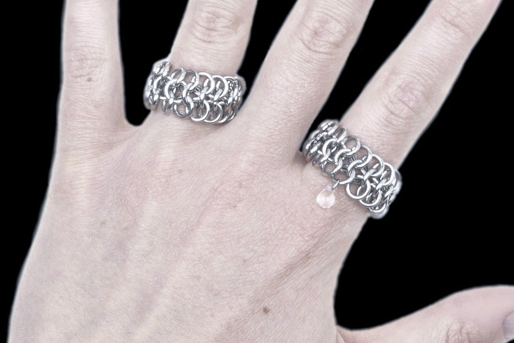 Hand wearing two silver chainmaille rings on a black background